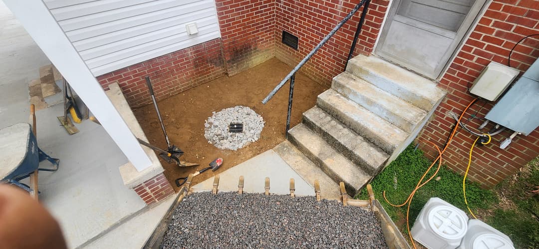 Construction site featuring new gravel, drainage system, and staircase near a brick house.