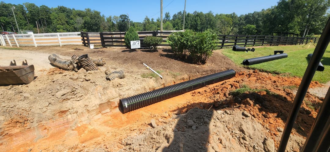 Drainage pipe installation in a landscaped area with dirt and tools visible.