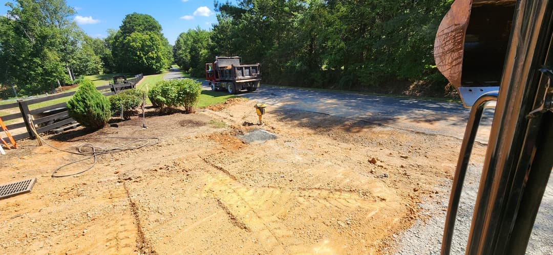 Construction site with excavated area, viewed from truck, surrounded by trees and road.