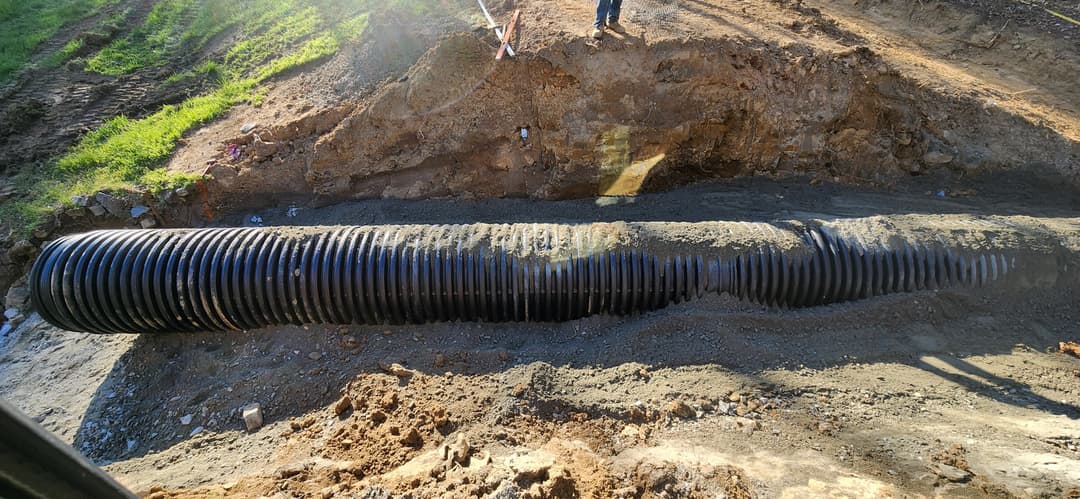 Black corrugated drainage pipe installation in a trench on a construction site.