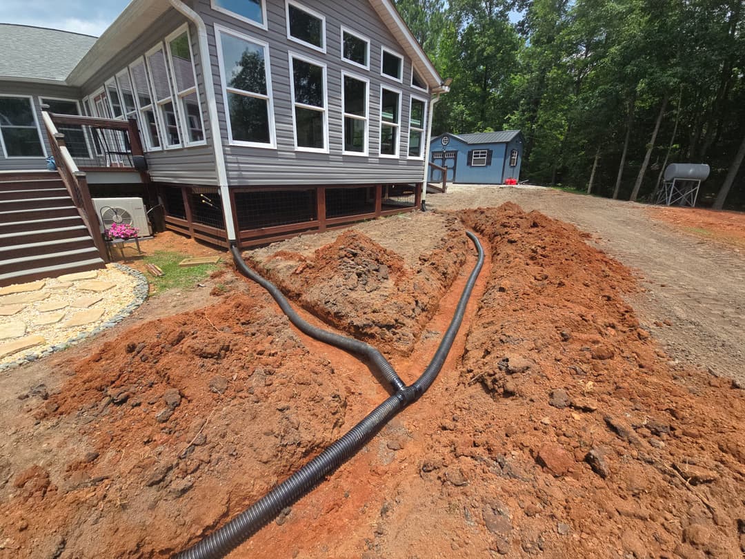 Residential yard with excavated soil and drainage pipes near a house and storage shed.