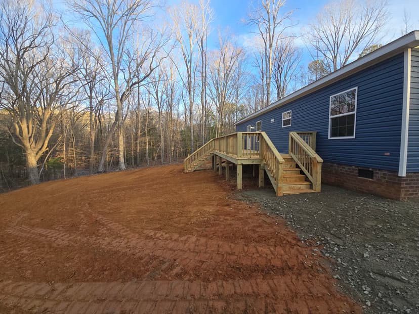 Newly built blue house with wooden steps, surrounded by bare trees and cleared land.