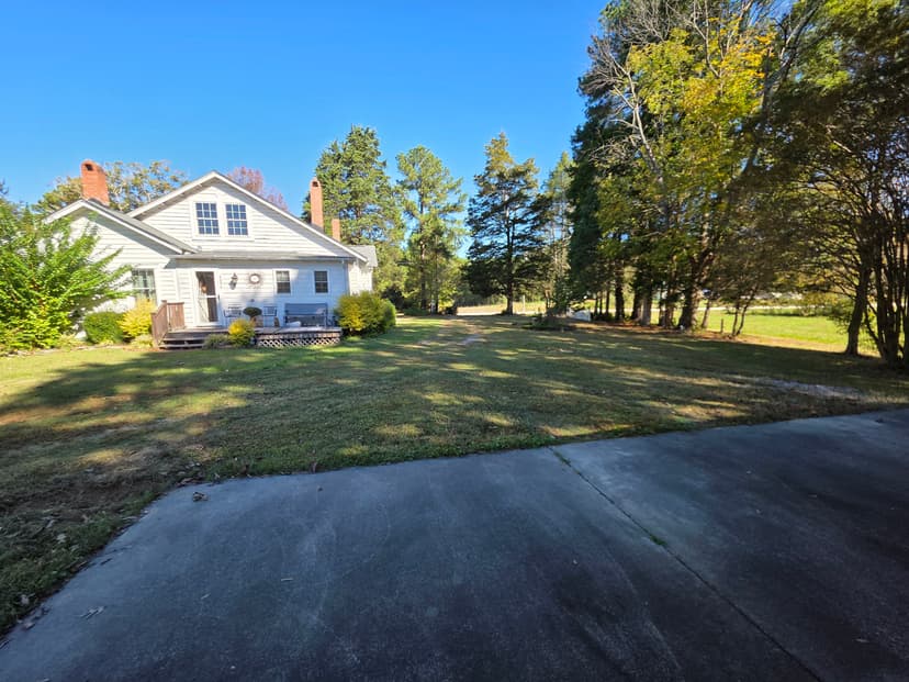 Charming house with a large yard and trees under a clear blue sky.