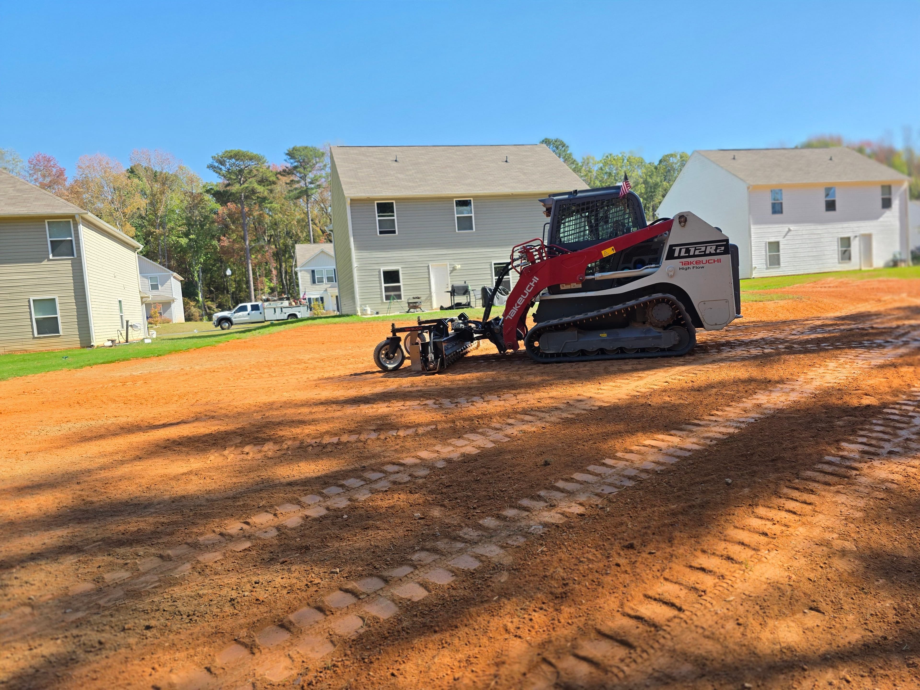 Skid steer loader preparing land for construction near residential homes on a sunny day.