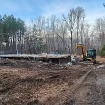 Construction site with excavator working on a foundation amid wooded area.