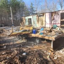Abandoned building site with debris and damaged structure surrounded by trees.