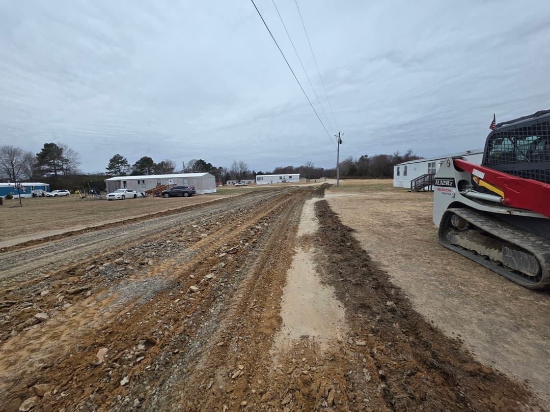 Construction site with heavy machinery and newly graded dirt road in rural area.