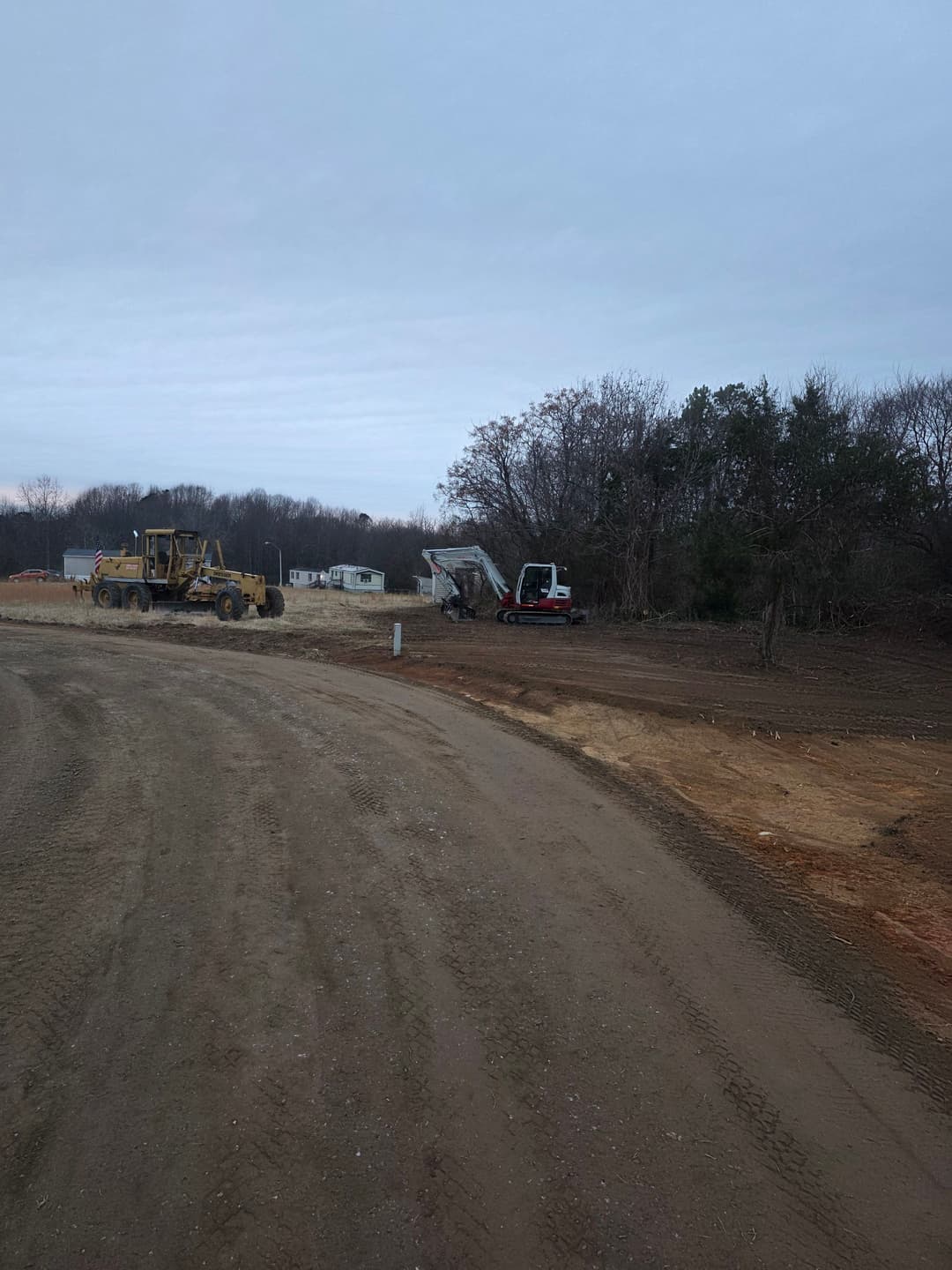 Construction site with heavy machinery and equipment on a dirt road under a cloudy sky.