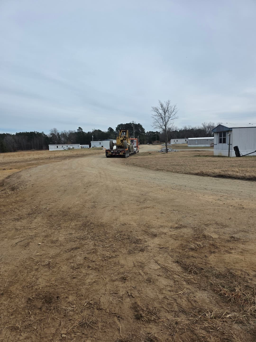 Heavy machinery truck on dirt road near industrial buildings in rural landscape.