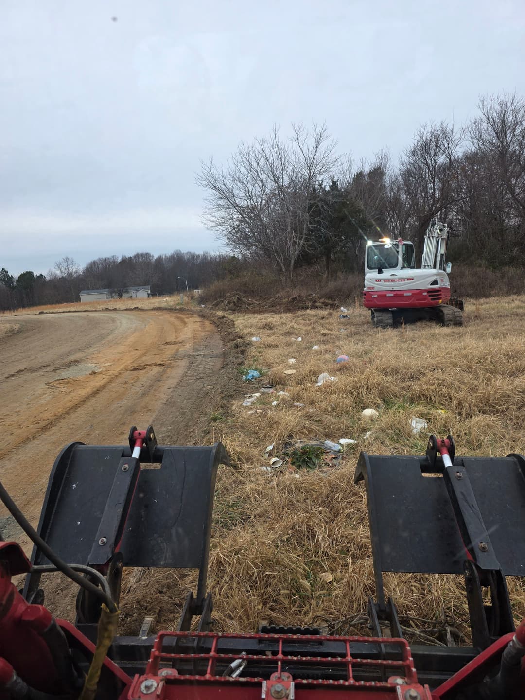 View from a tractor's front, showing overgrown field and waste along the roadside.