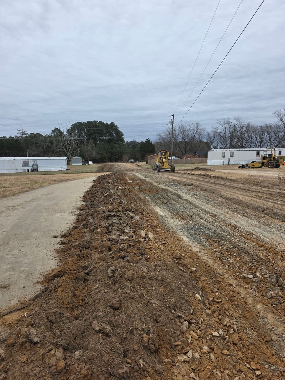 Construction site showing a newly graded road and heavy machinery on an overcast day.