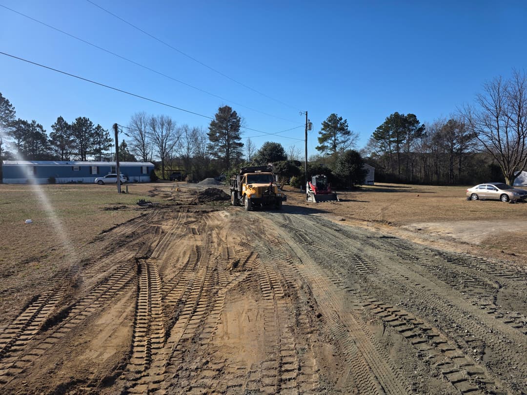 Construction site with heavy machinery working on a dirt road in a rural area.