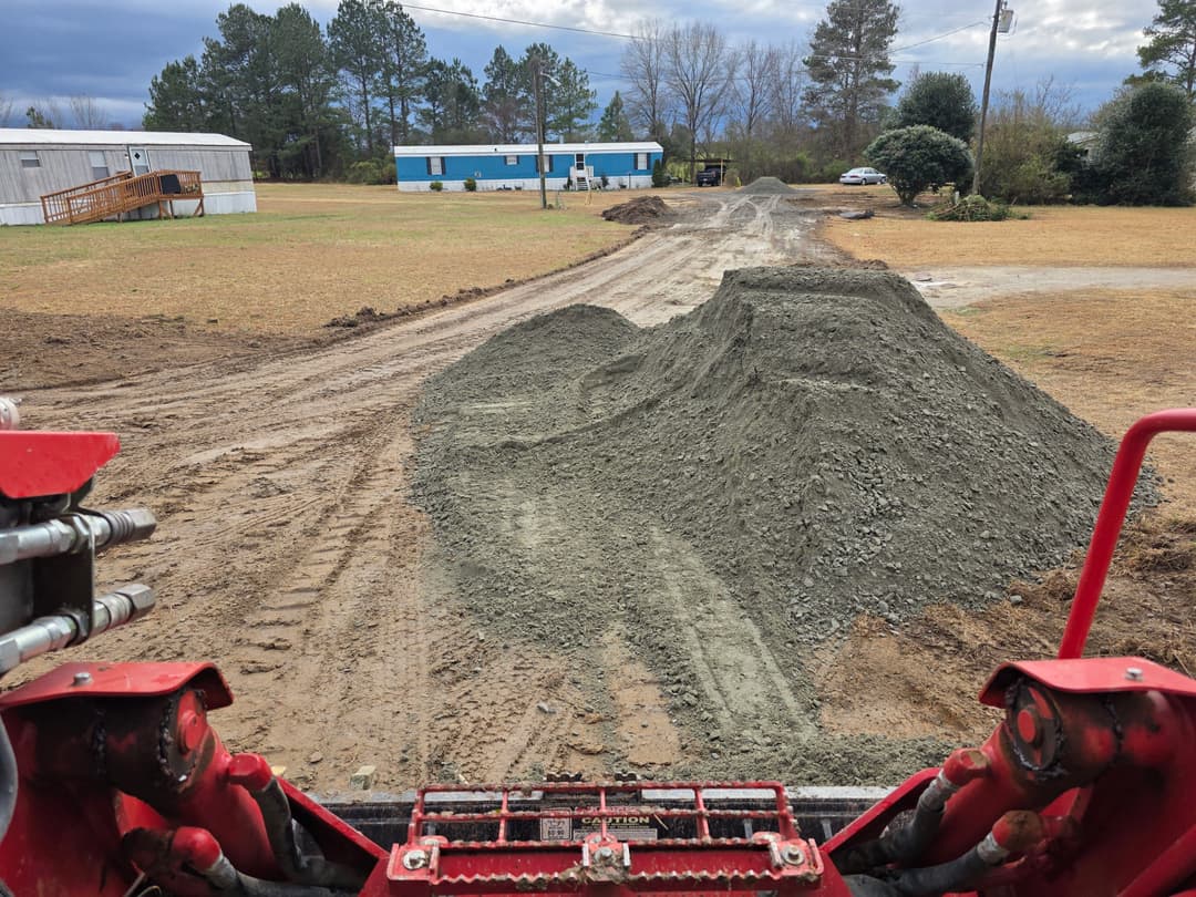 View from a construction vehicle showing a gravel path leading to a residential area.