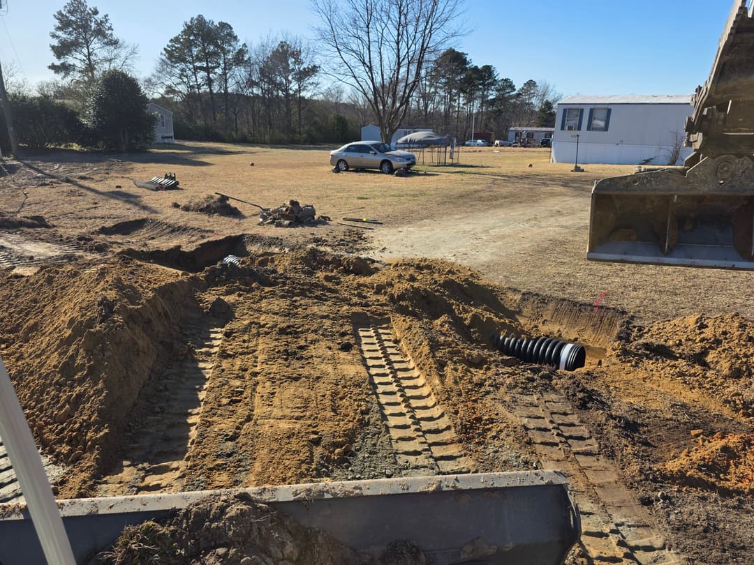 Excavation site with machinery tracks, dirt piles, and a parked car in a rural area.