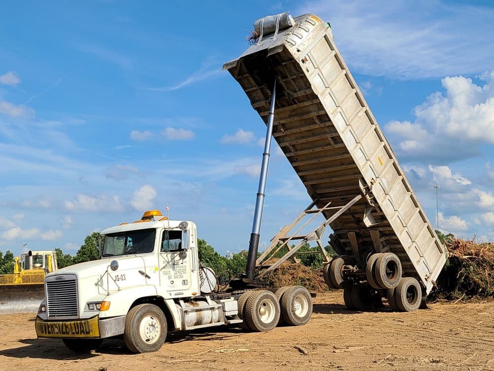 Dump truck unloading debris at a construction site under a clear blue sky.