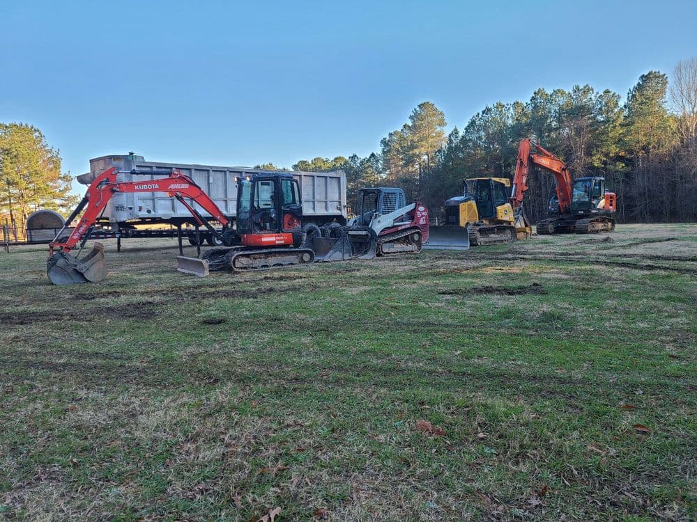 Construction site with various excavators and machinery on a grassy field.