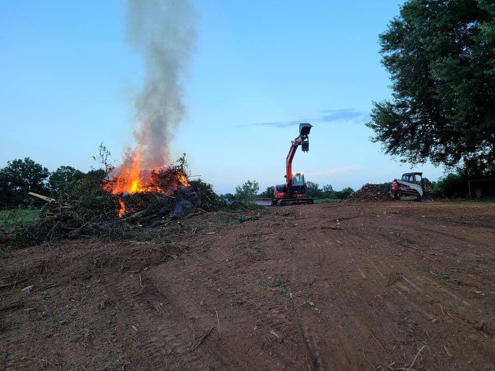 Controlled burn of debris with machinery operating in a rural landscape at dusk.