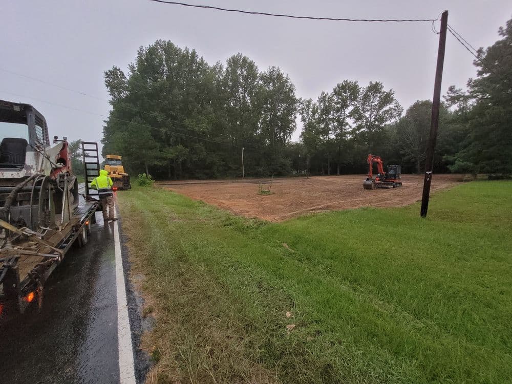 Construction site preparation with machinery and workers alongside a wet road.