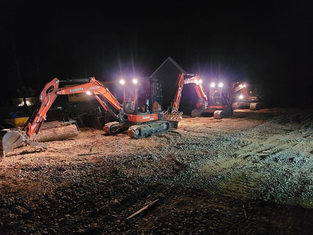 Excavators with headlights illuminate a construction site at night.