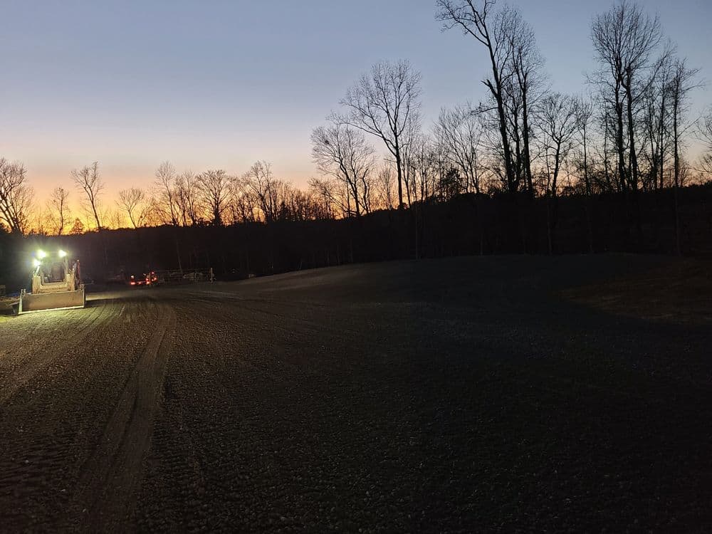 Construction site at sunset with equipment and trees silhouetted against the sky.