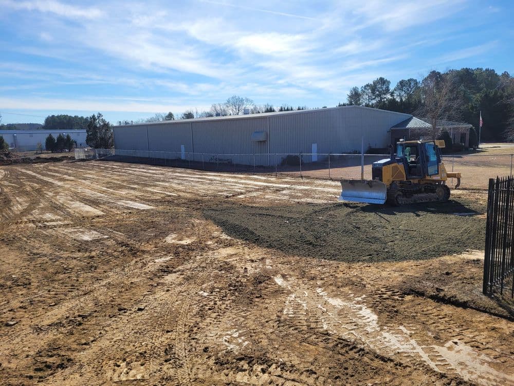 Bulldozer leveling land at a construction site with a warehouse in the background.