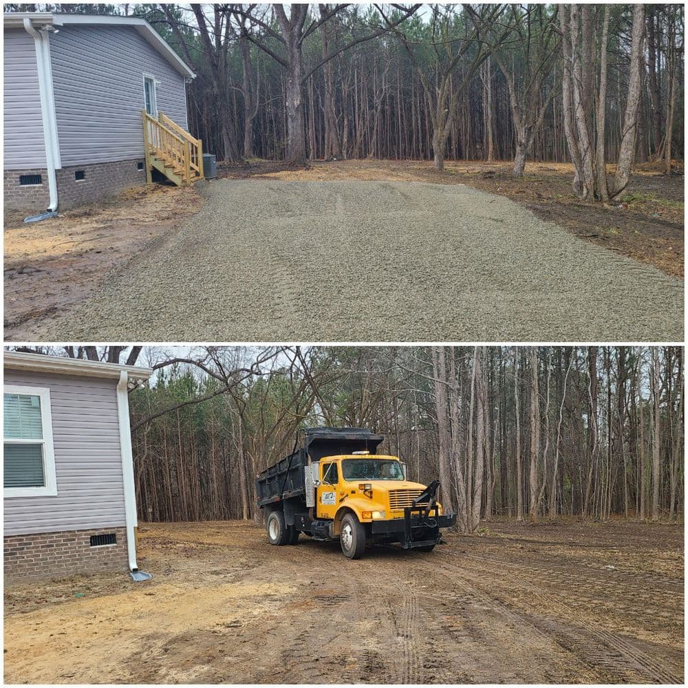 Gravel driveway installation near a house with a dump truck in a wooded area.