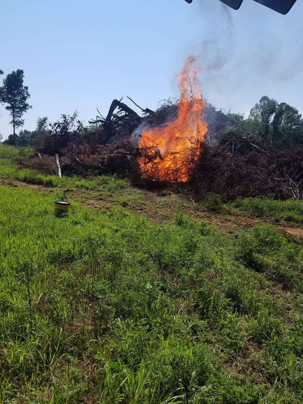 Controlled burn of brush pile in green field under clear blue sky.