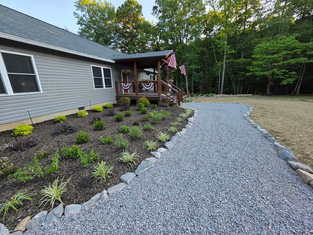 Gravel walkway leading to a house with garden and American flags on the porch.