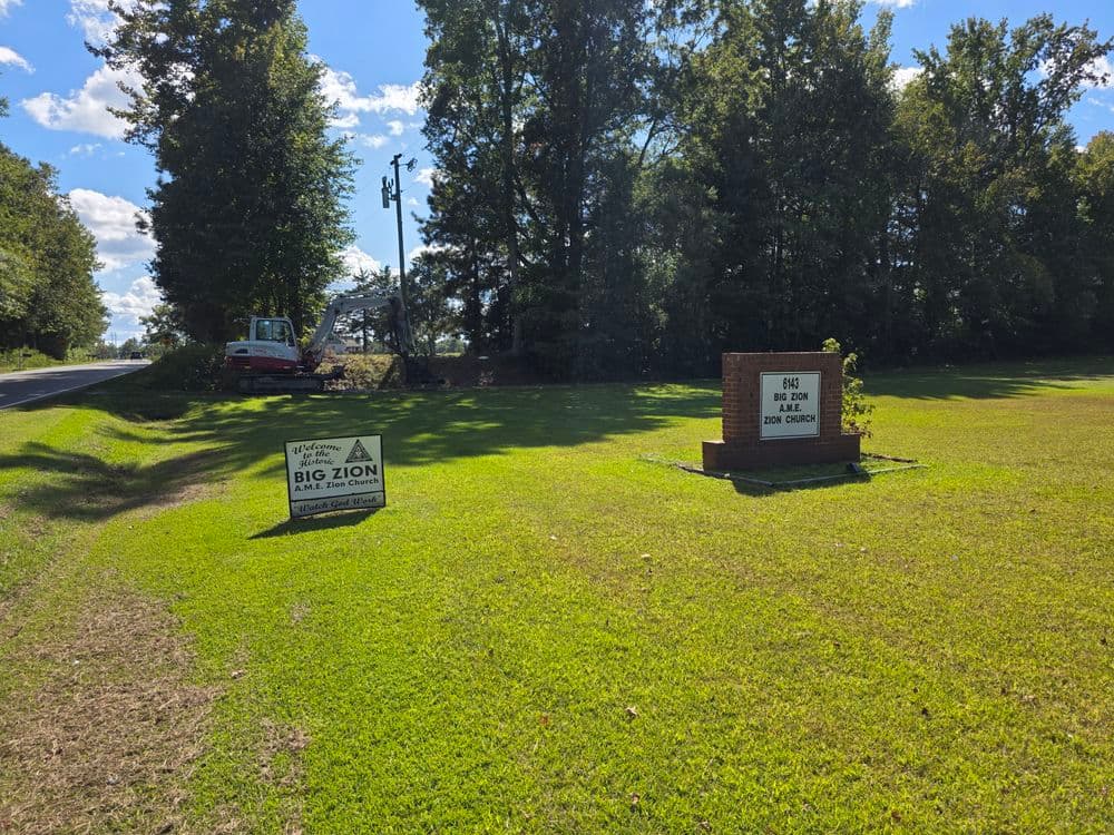 Big Zion Church sign near a road surrounded by trees on a sunny day.
