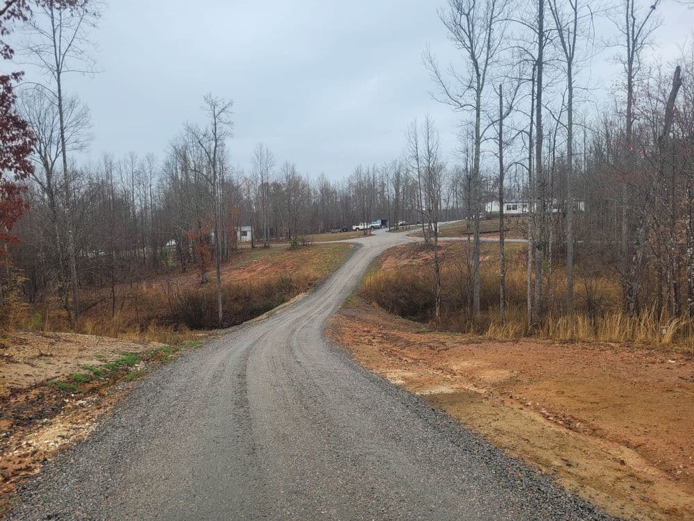 Gravel road winding through bare trees to mobile homes in a rural area.