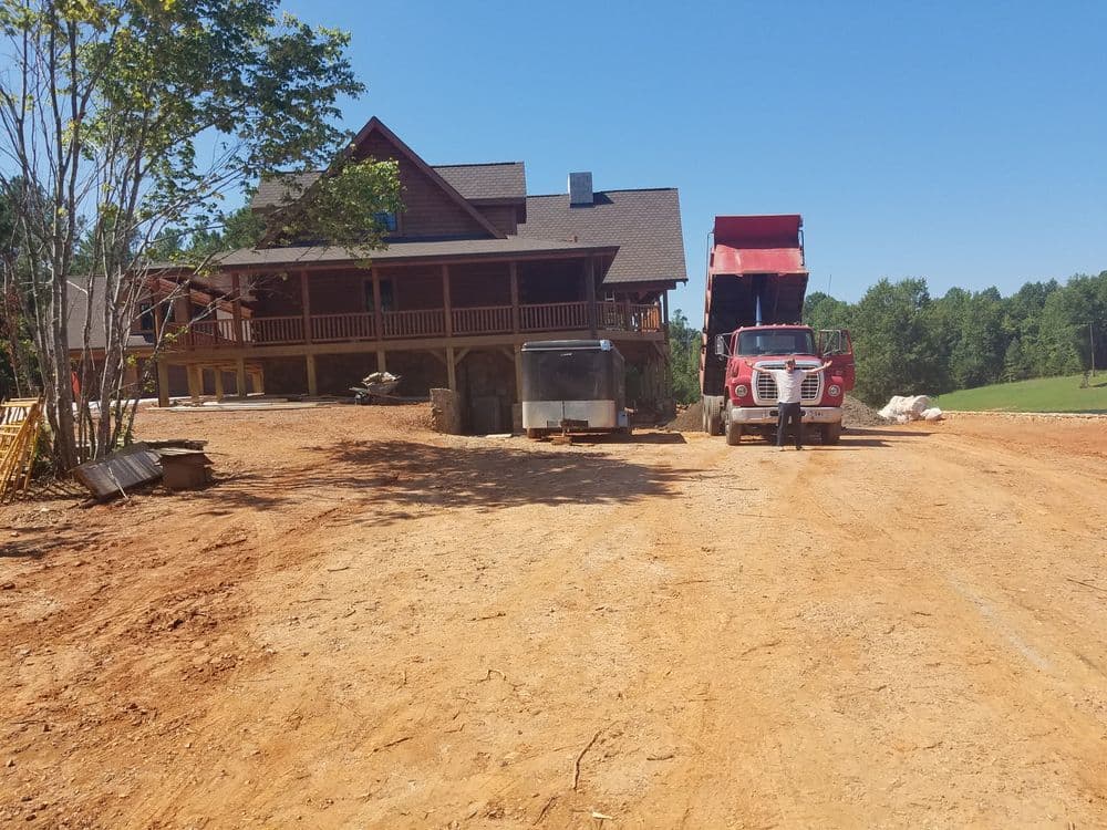 Construction site with a red dump truck and a new large wooden house under development.