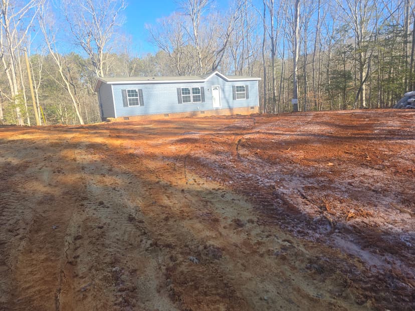 New mobile home on cleared lot surrounded by trees, ready for landscaping and development.