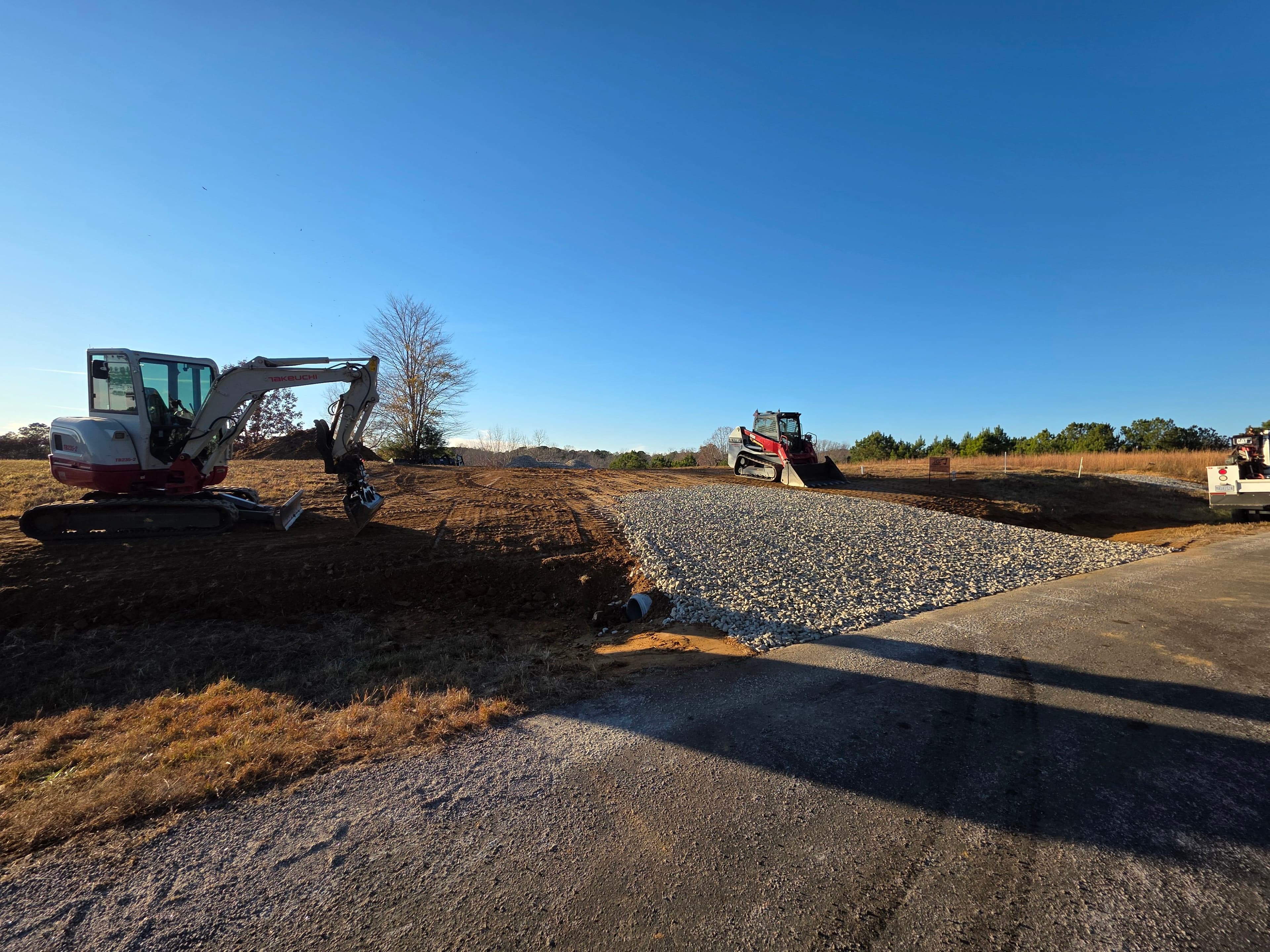 Construction site with excavator and heavy machinery on gravel surface under clear blue sky.