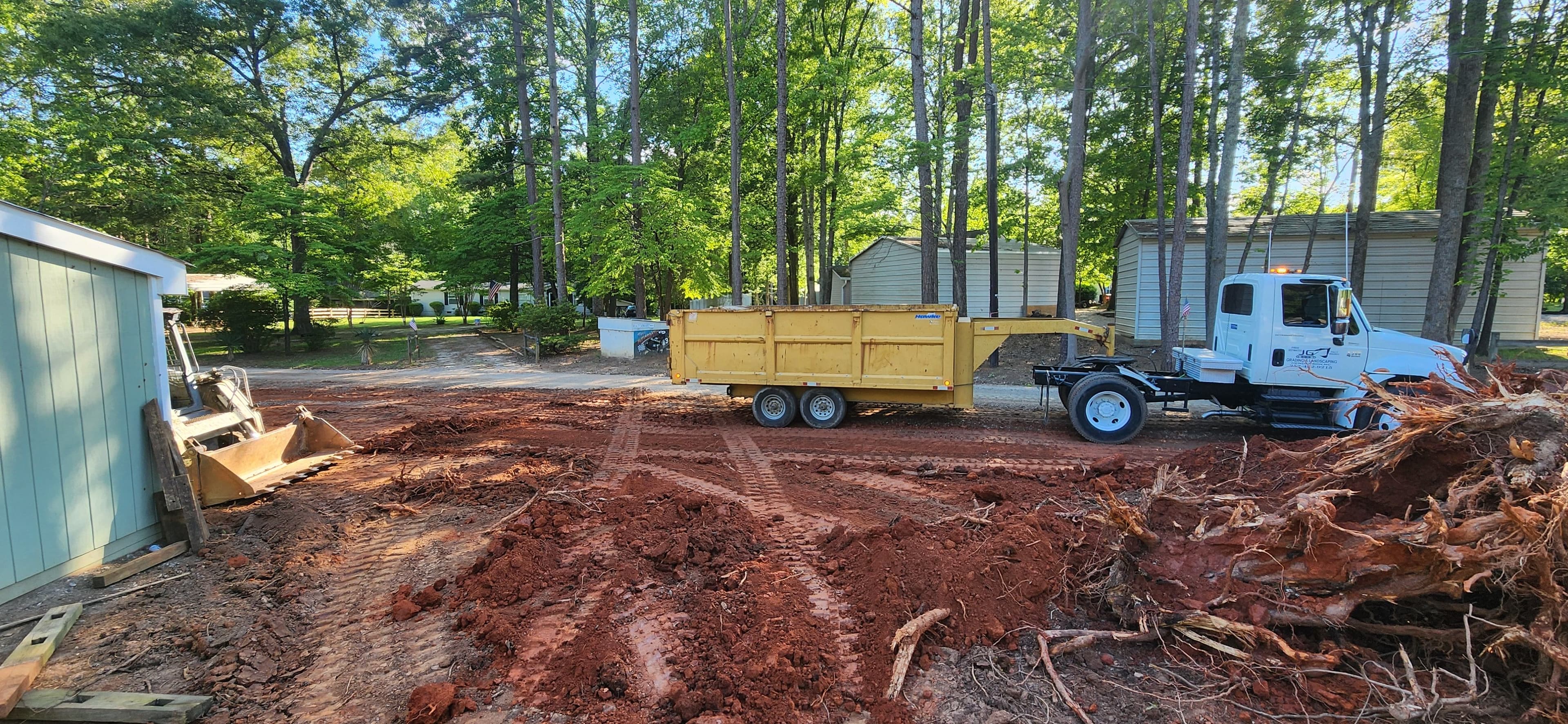 Construction site with a dump truck and bulldozer amid cleared trees and red soil.