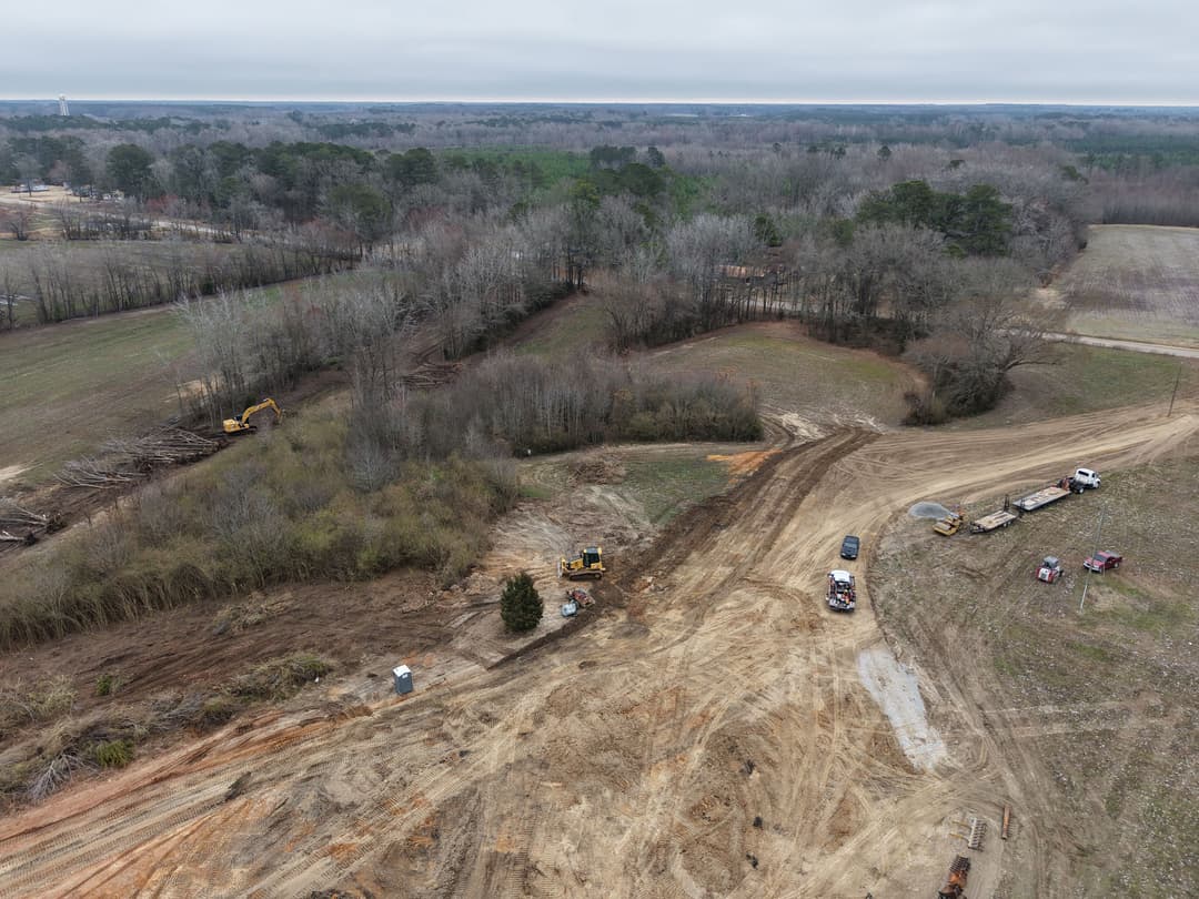 Aerial view of construction site with heavy machinery and cleared land in rural setting.