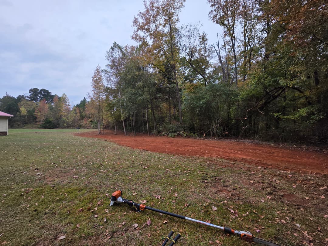 Landscaping tools on a freshly cleared red dirt path through autumn foliage.