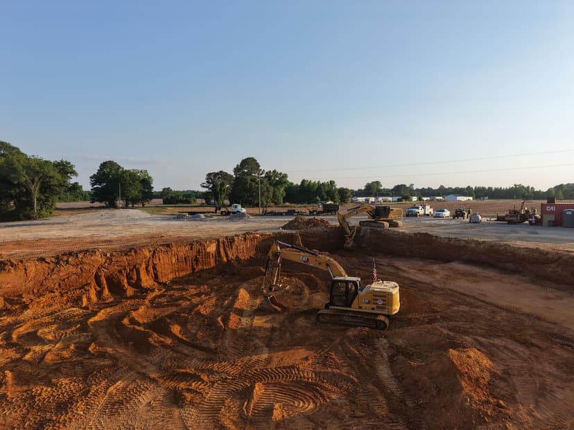 Excavator working on a construction site with cleared land and machinery in the background.