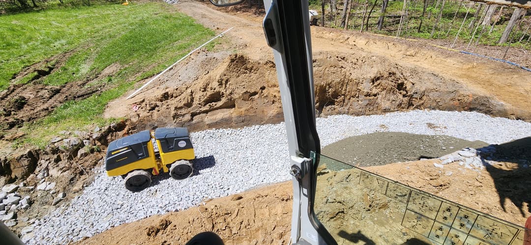 View from an excavator showing a construction site with a mini dumper and gravel path.