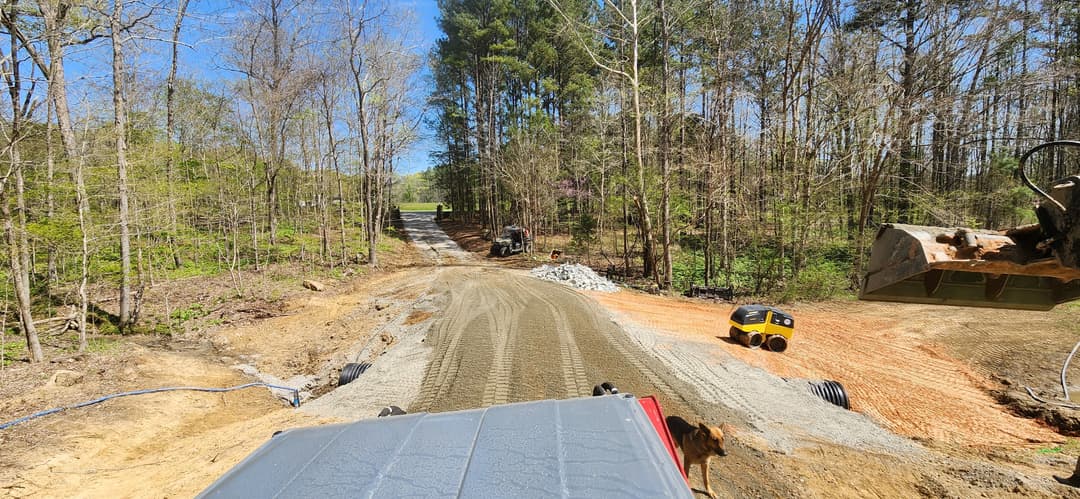 Construction site in a forested area with machinery and a newly graded road.