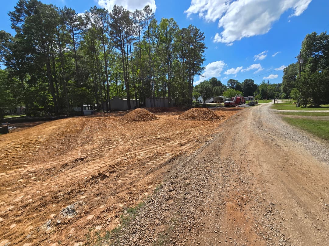 Construction site with cleared land, gravel road, and trees under a clear blue sky.