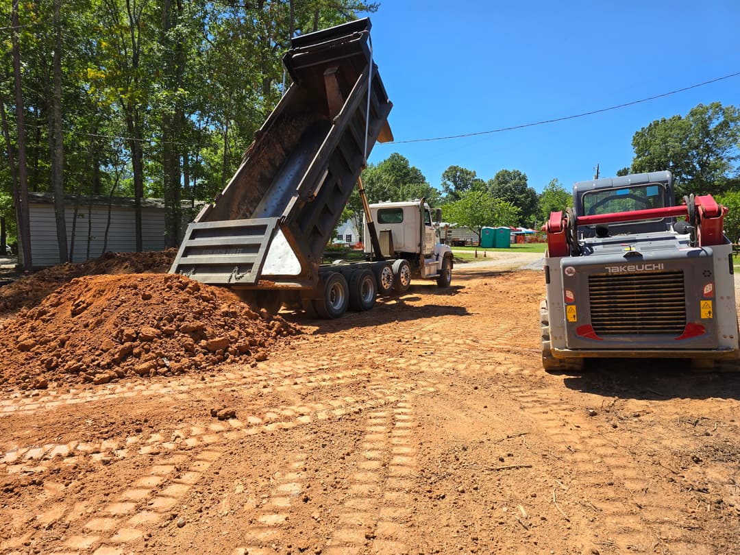Dump truck unloading soil on construction site with heavy machinery in background.