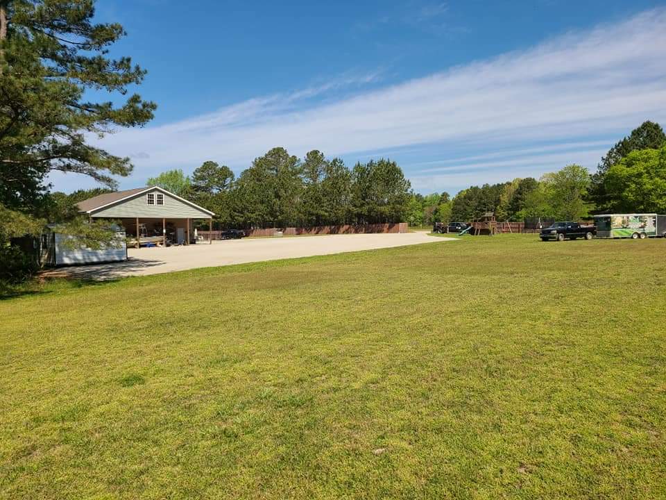Spacious outdoor area with a pavilion, green grass, and parked vehicles under blue sky.